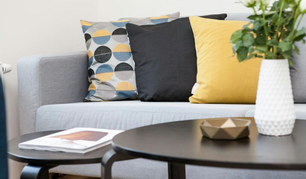 Modern living room with a light gray sofa, colorful pillows, and black coffee tables with a vase and a small bowl.