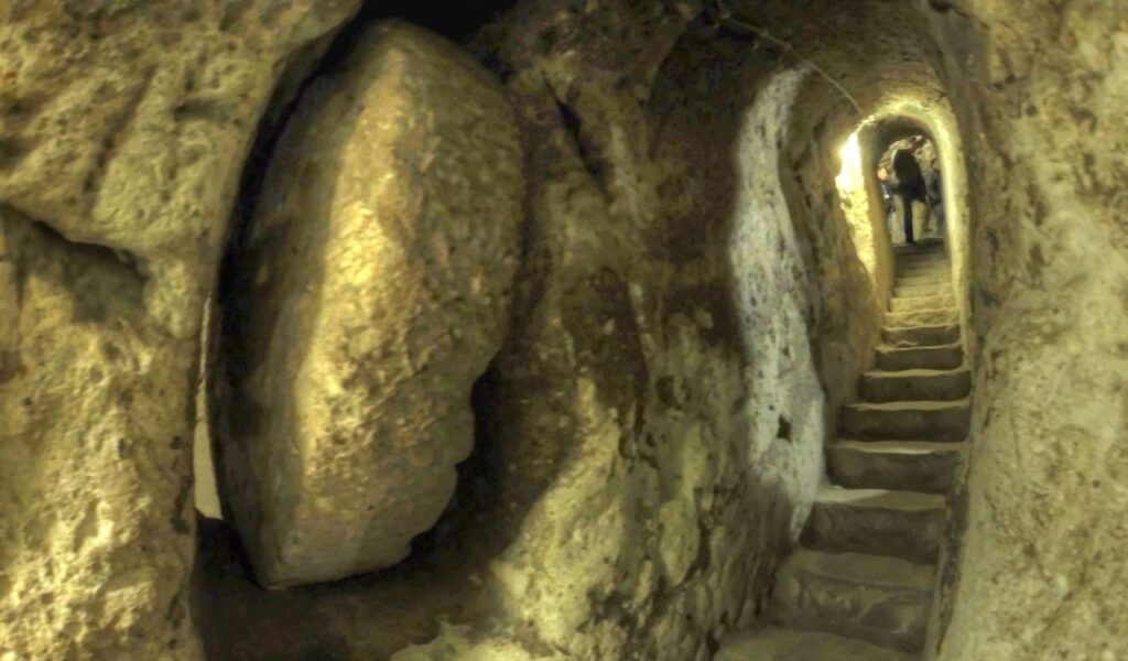 Narrow stone staircase and tunnel inside Derinkuyu underground city in Turkey, with visitors exploring the ancient passage.