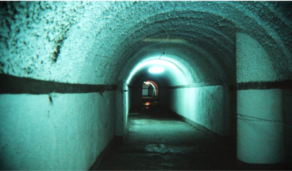 Dimly lit tunnel inside Dixia Cheng underground city in Beijing, China, with curved ceiling and concrete walls illuminated in blue.
