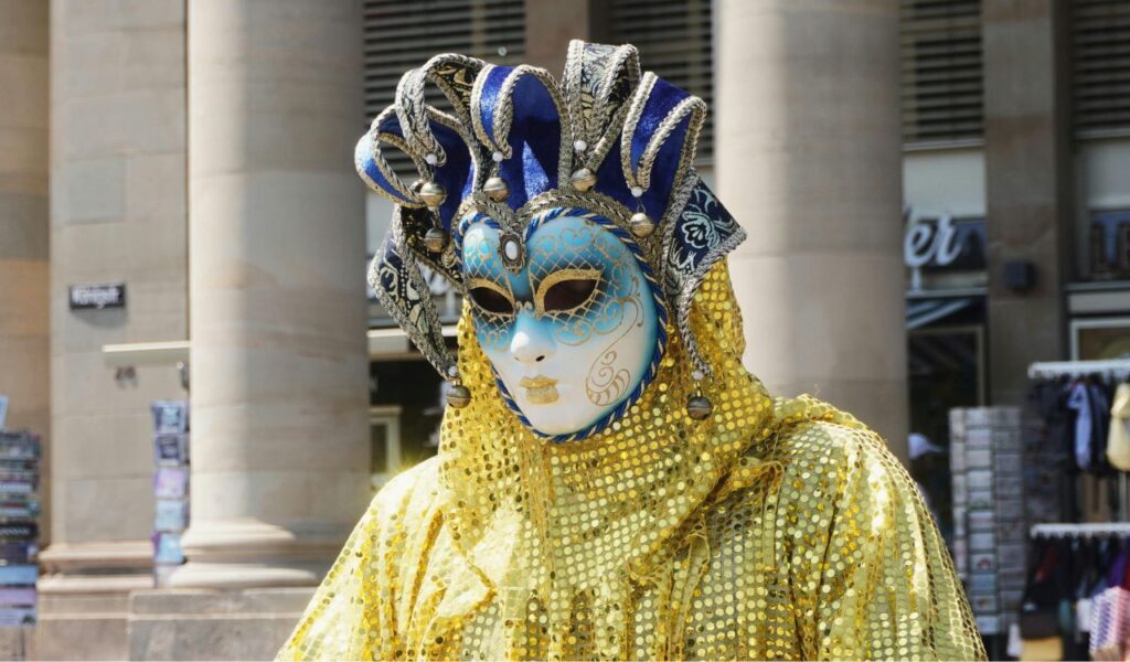 Venetian carnival performer in a colorful golden and blue mask with a glittering yellow costume.