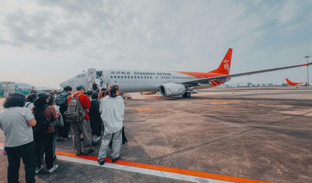 Passengers lining up to board a Shenzhen Airlines flight on the tarmac, with the airplane in the background.