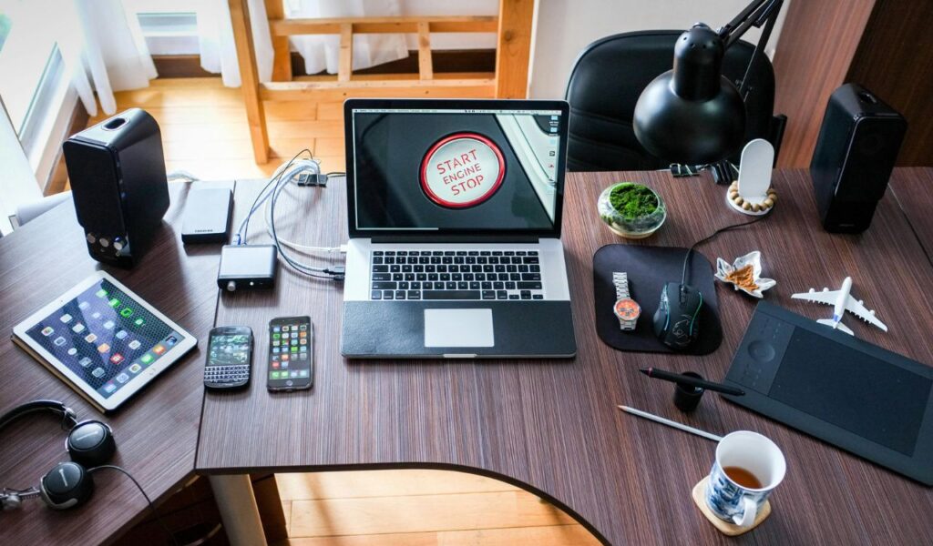 Modern workspace with a laptop, smartphones, tablet, gadgets, and accessories neatly arranged on a wooden desk.