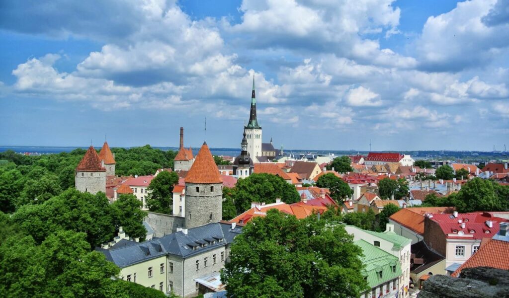 Scenic view of Tallinn, Estonia featuring medieval towers, red rooftops, and a tall church spire surrounded by greenery.