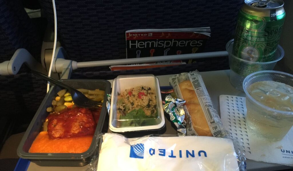Economy class meal tray with entrée, salad, bread, and drinks, showing standard in-flight meal and beverage service.