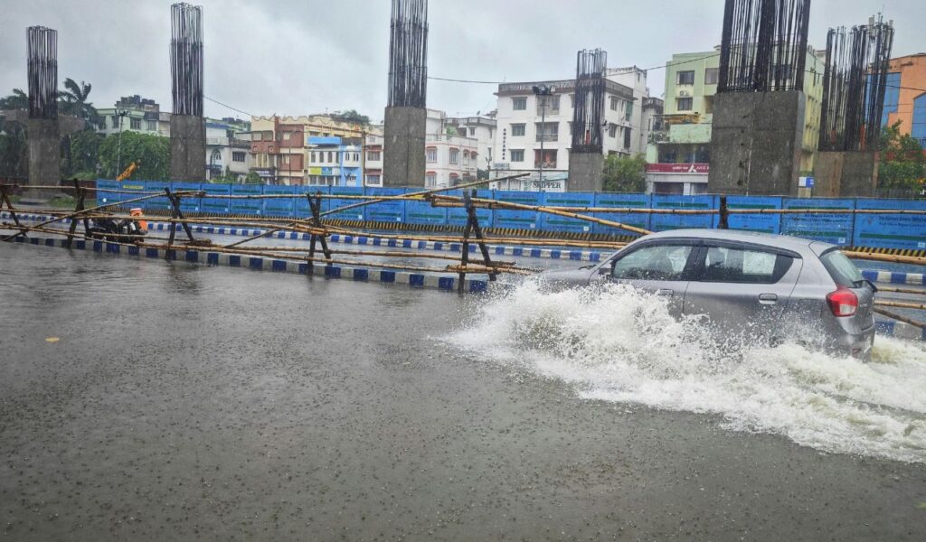 A car driving through a flooded urban street during heavy rain, illustrating unexpected road trip emergencies and weather-related travel challenges.