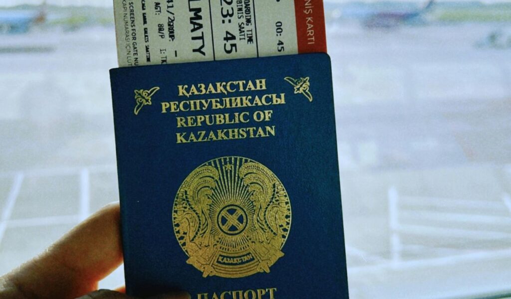 Close-up of a Kazakhstan passport and boarding pass at the airport with a view of the airplane in the background.