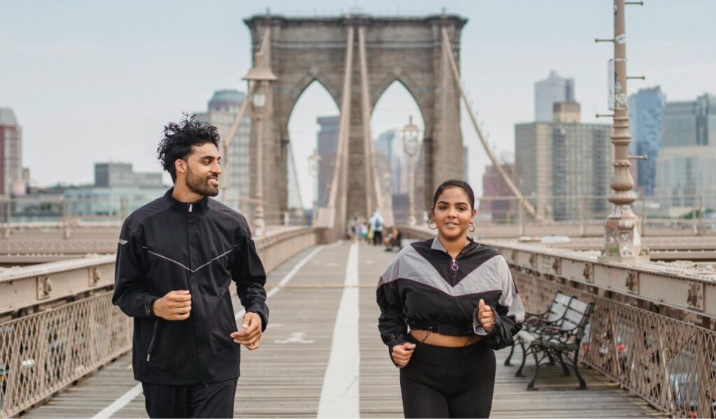 Man and woman jogging together on a city bridge, staying active and energized during travel for wellness