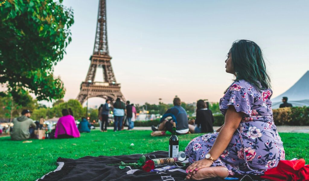 Woman enjoying a romantic picnic with wine near the Eiffel Tower in Paris, capturing the essence of date night in France.