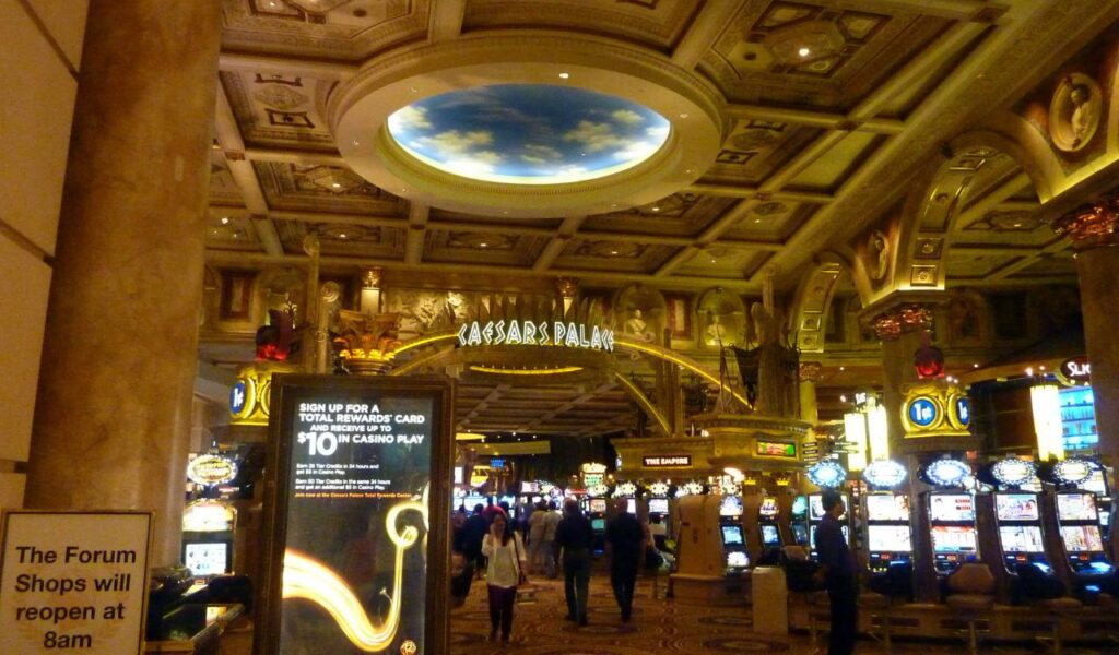 Interior of Caesars Palace casino with ornate ceilings, slot machines, and a sign about The Forum Shops reopening at 8 a.m.