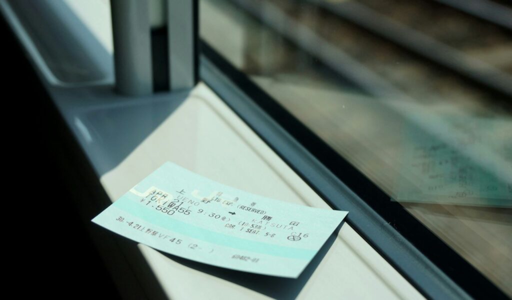 A Japanese train ticket rests on a windowsill inside a moving train, with blurred train tracks visible outside the window.