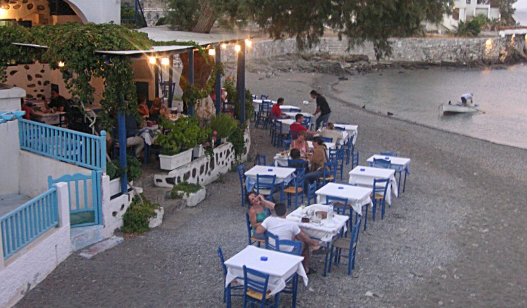 Romantic beachfront dining at a Greek taverna with white tablecloths, blue chairs, and sea views perfect date night setting.