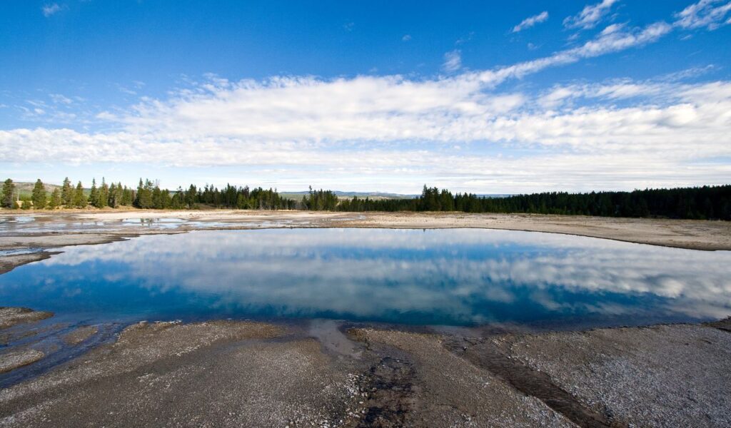 Tranquil lake in Haiti reflects the sky and forest under a clear blue sky.