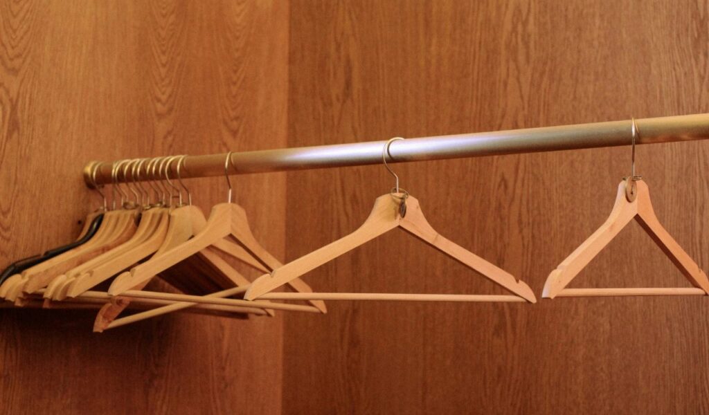 Wooden clothes hangers neatly arranged on a metal rod inside a wooden closet, ready for hanging garments.