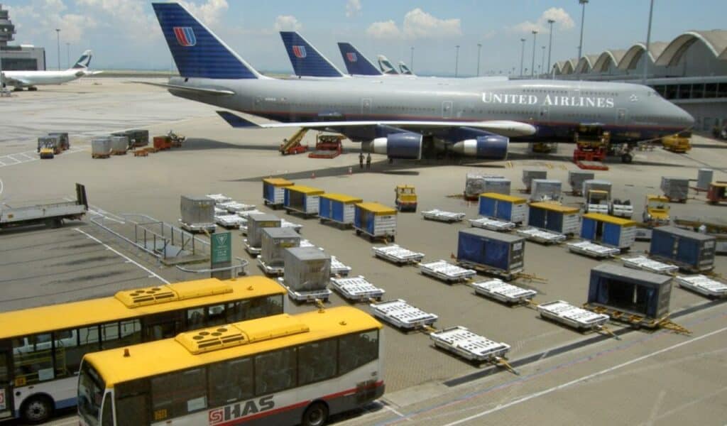 United Airlines aircraft parked at Hong Kong International Airport with airport ground support equipment, cargo containers, and shuttle buses in view on the tarmac.