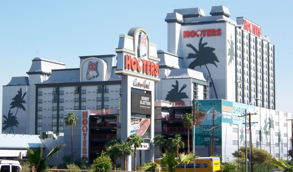 Exterior of a Hooters restaurant and hotel with large signage, palm tree graphics, and visible branding.