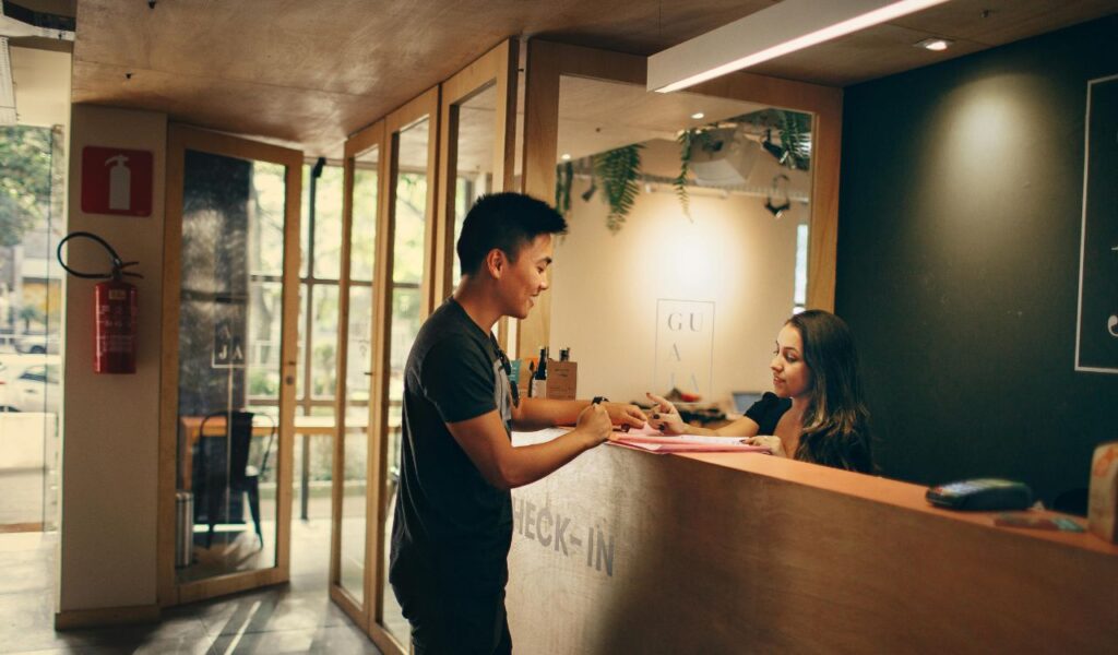 Man checking in at hotel front desk while staff explains paperwork, suggesting possible discussion of extra fees.