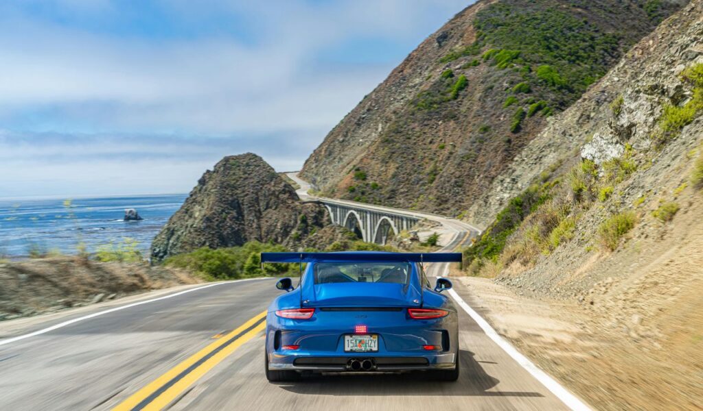 Blue sports car driving along a scenic coastal highway with cliffs and ocean views, symbolizing long-distance road travel.