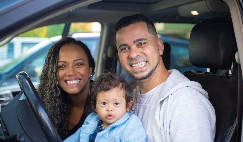 Smiling family of three sitting inside a car, ready for a road trip, showcasing group travel dynamics.