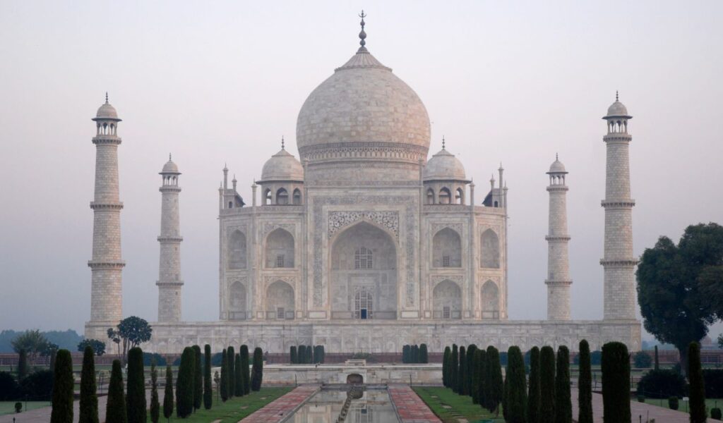The Taj Mahal, an iconic white marble mausoleum with a large central dome and four minarets, stands symmetrically amid manicured gardens in Agra, India.