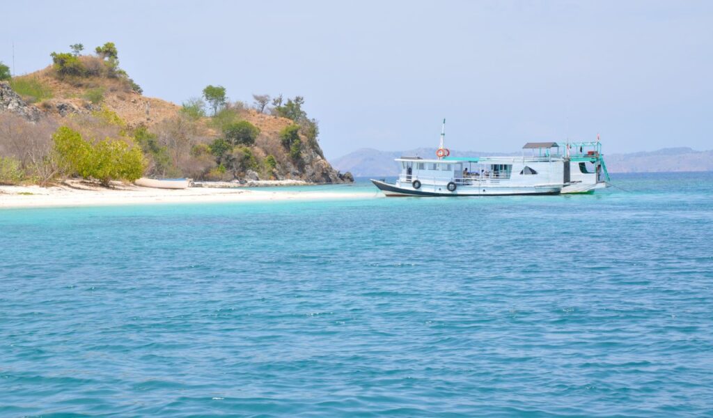 A small boat anchored near a tropical beach with clear turquoise waters in Indonesia.