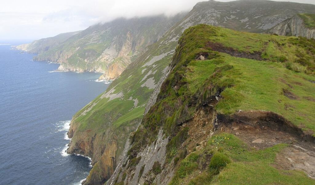 Scenic view of Ireland's coastline with lush green hills and dramatic cliffs overlooking the Atlantic Ocean.