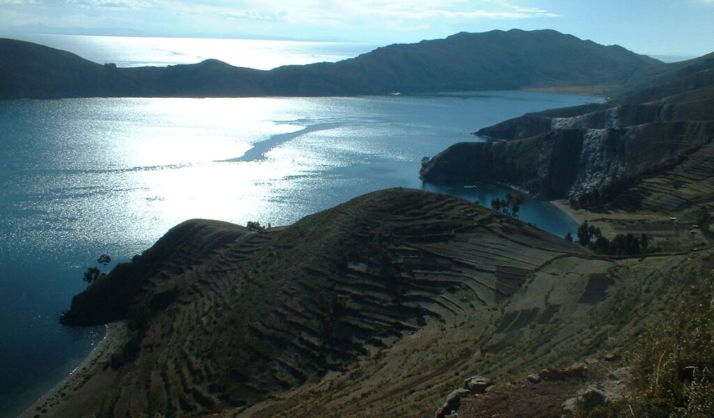 Terraced hills overlooking Lake Titicaca at Isla del Sol, Bolivia, under a bright sky.
