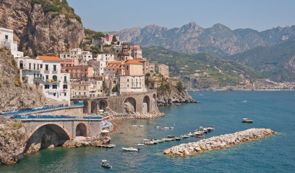 Colorful cliffside buildings and curving coastal road along Italy’s Amalfi Coast with boats in the turquoise sea.