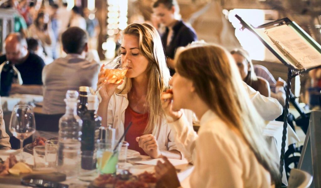 Two women enjoying drinks and food at a lively Italian restaurant, capturing the romantic, social vibe of dining in Italy.