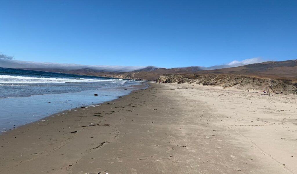 Wide sandy shoreline and gentle waves at Jalama Beach near Lompoc under a clear blue sky.