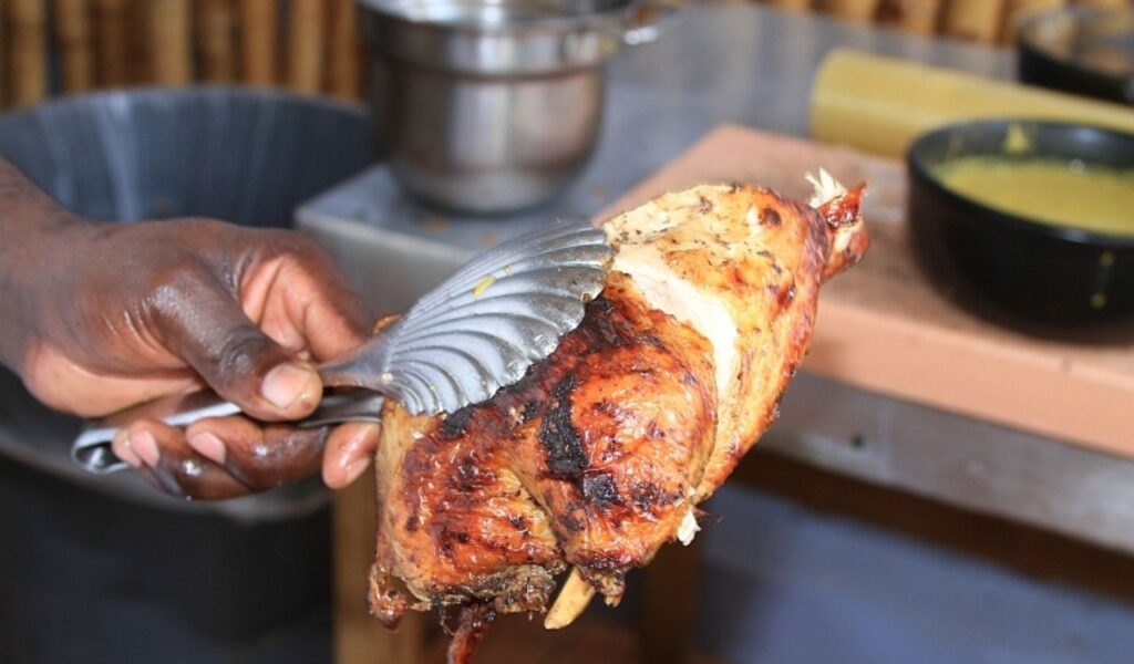 Grilled Jamaican jerk chicken held with tongs at a street food stall.