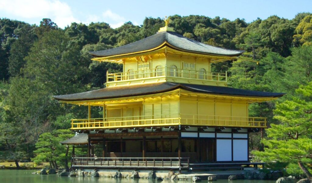 Kinkaku-ji, the Golden Pavilion in Kyoto, Japan, a Zen Buddhist temple covered in gold leaf, reflects peacefully on the surrounding pond and lush greenery.