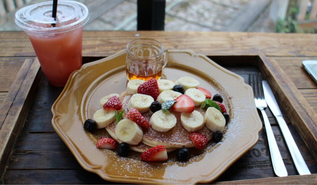 Japanese-style breakfast with fruit-topped pancakes, syrup, and juice—perfect for a cozy and romantic morning meal.