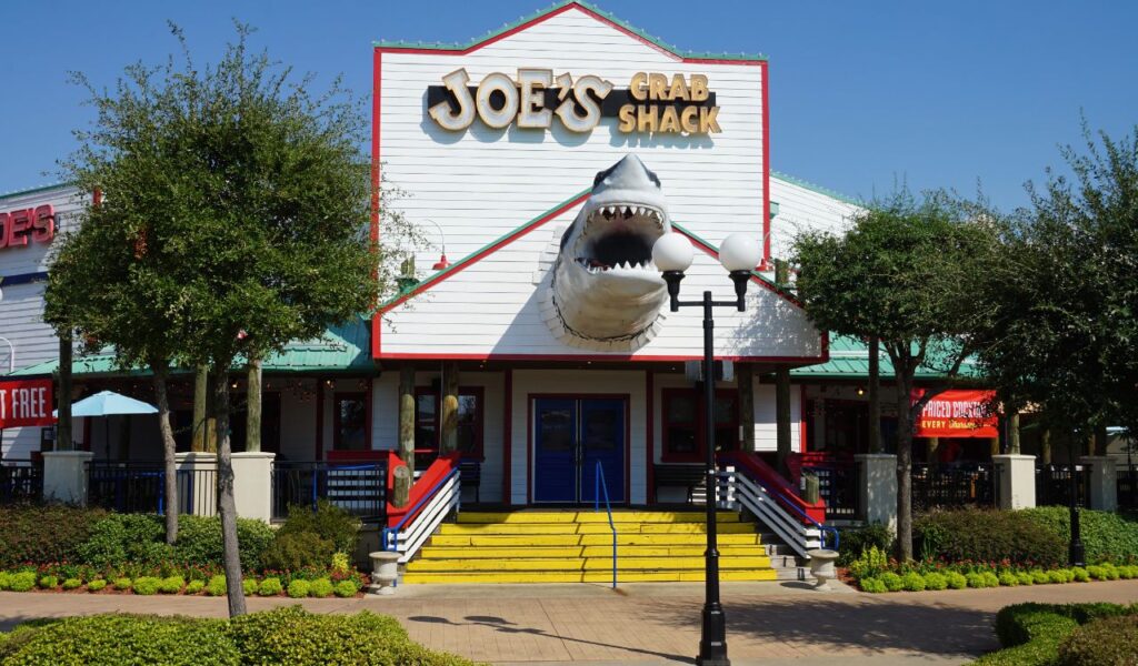 Exterior of Joe's Crab Shack with its signature shark entrance design and vibrant outdoor setting surrounded by trees and greenery.