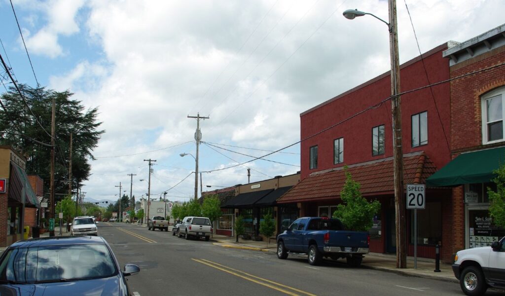 A quiet street in downtown Carlton, Oregon, lined with small shops and parked cars under a partly cloudy sky.