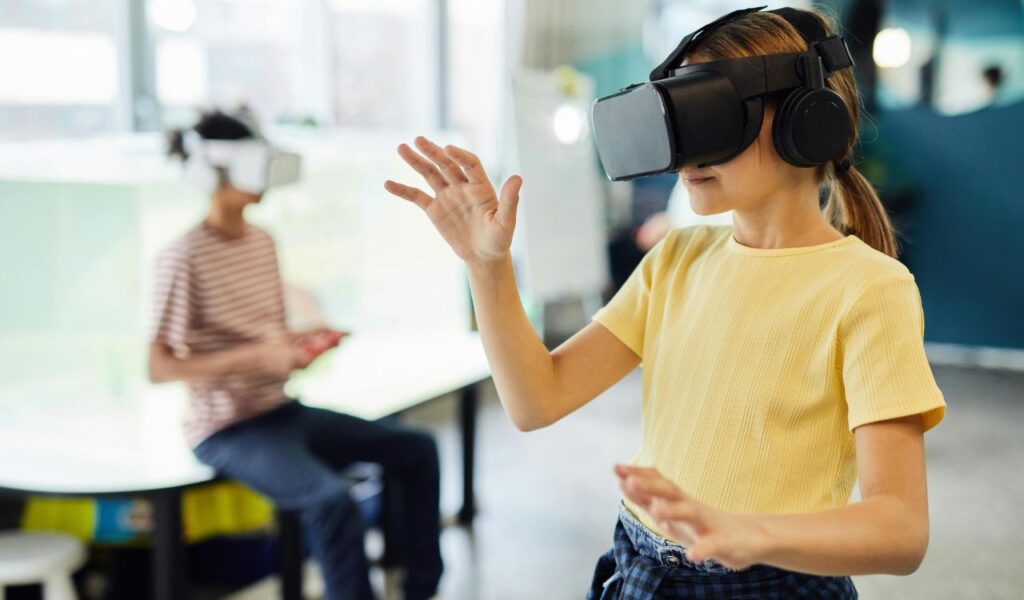 Young girl using a VR headset in an interactive play area while another child explores virtual reality in the background.