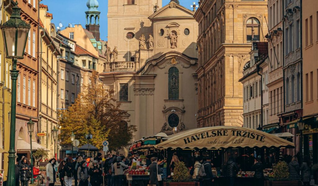 Crowds gather at Prague’s historic Havel Market surrounded by old buildings, highlighting local Czech culture and charm.