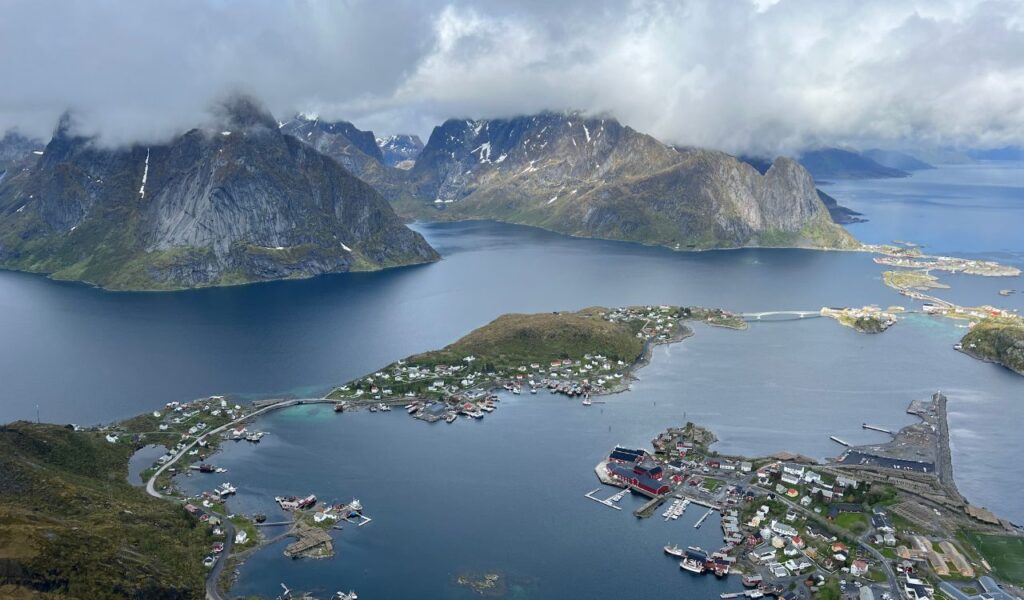 Aerial view of the Lofoten Islands in Norway with dramatic mountains, coastal villages, and blue fjords under low-hanging clouds.