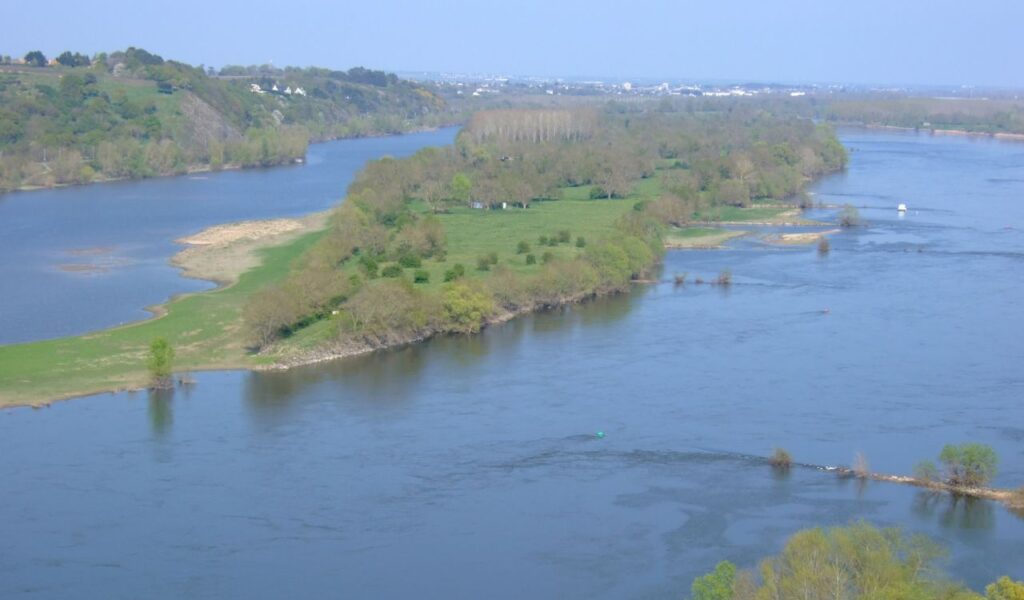 Aerial view of a lush green river island along the Loire River in France, with distant hills and scattered villages.
