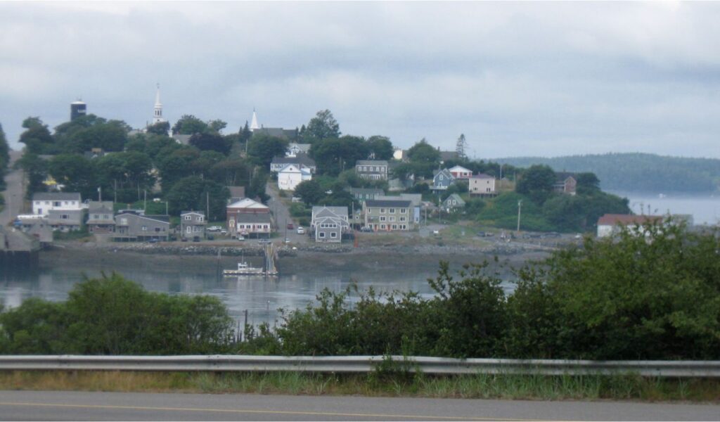 Coastal town of Lubec, Maine with colorful houses, church steeples, and calm harbor waters under a cloudy sky.