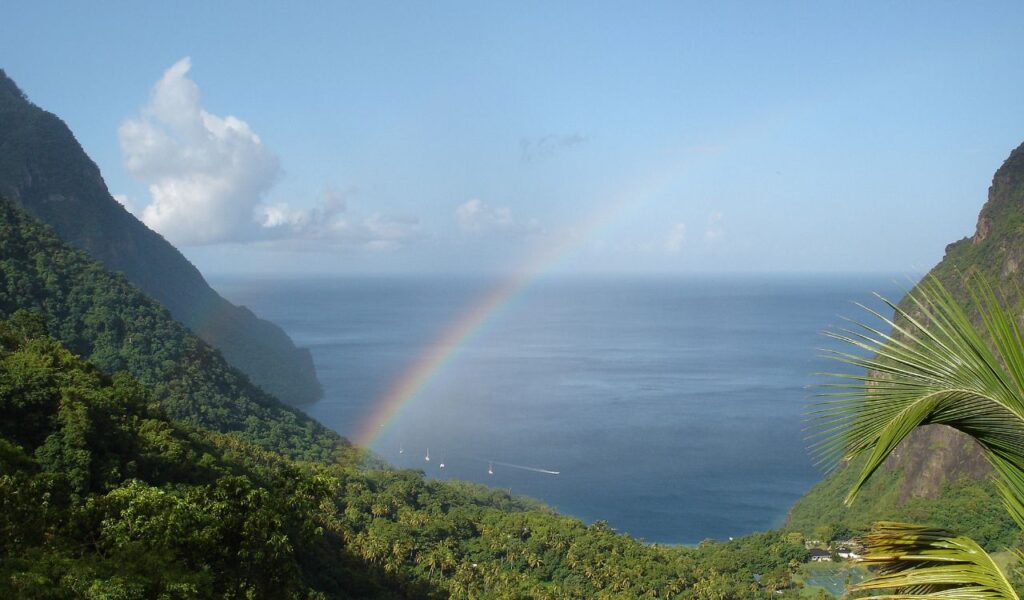 Rainbow over lush green hills and ocean bay in Saint Lucia, framed by steep volcanic peaks.