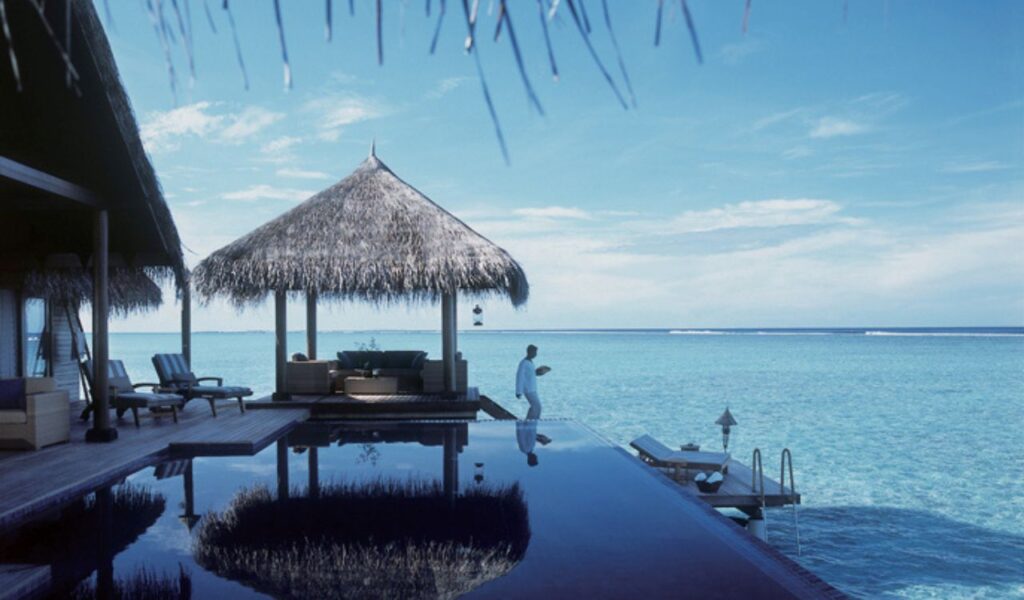 Luxury overwater villa in the Maldives with thatched roofs, a private pool, and clear turquoise ocean views.