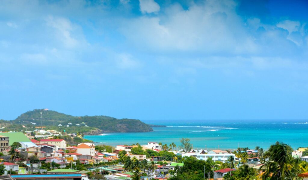 Colorful coastal town in Martinique with bright rooftops, lush greenery, and turquoise Caribbean Sea in the background.