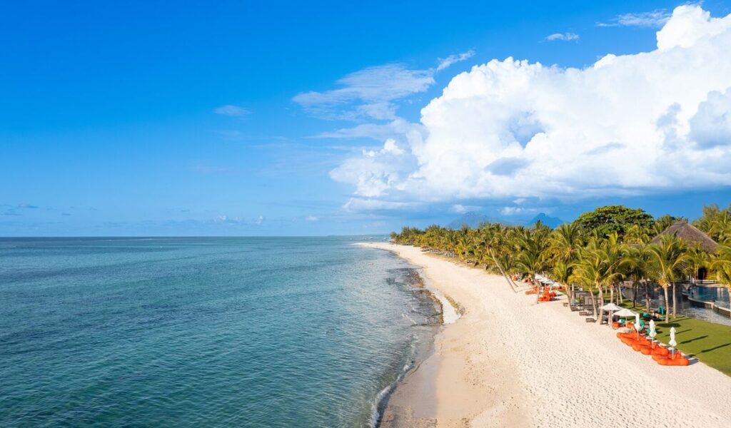 Scenic beach in Mauritius with clear blue water, palm trees, and colorful lounge chairs under a sunny sky.