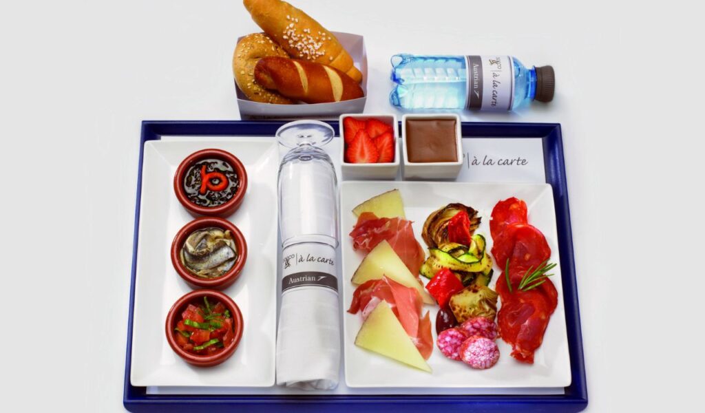 A healthy, balanced in-flight meal tray with light meats, cheese, grilled veggies, fruits, and water for mindful eating..