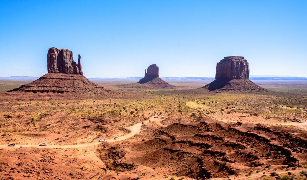 Scenic view of Monument Valley, Utah, with iconic sandstone buttes rising from the desert under a clear blue sky.
