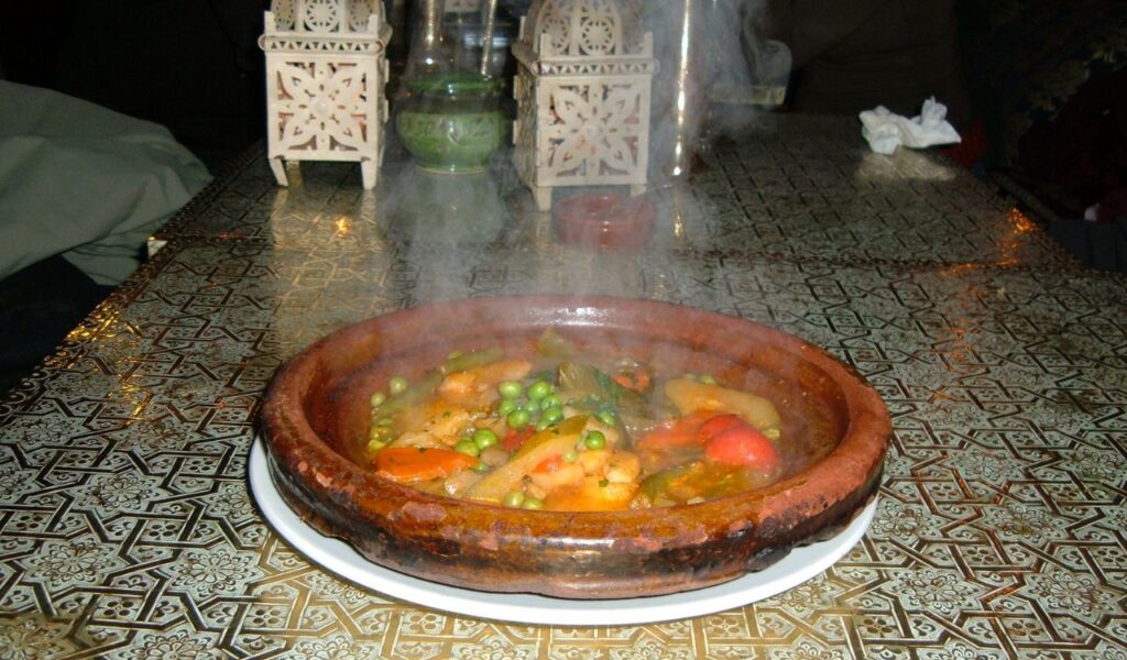 Traditional Moroccan tajine stew served hot in a clay dish, filled with vegetables and spices on a patterned table.