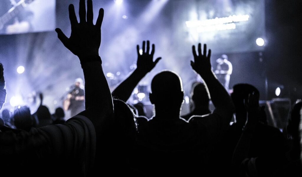 A crowd at a live concert raising their hands in excitement, enjoying the music and atmosphere under stage lights.
