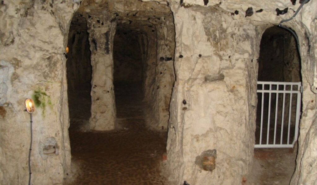 Stone passageways and columns inside the Naours underground city in France, with dim lighting and gated tunnel entrances.