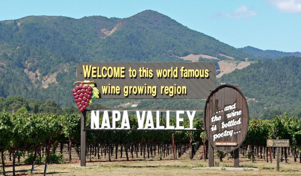 Welcome sign for Napa Valley in front of a vineyard with mountains in the background.