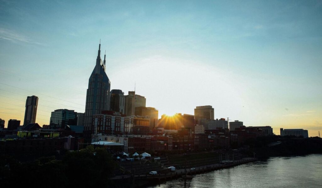 Sunset over the Nashville skyline with city buildings and the river in the foreground.